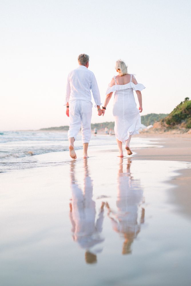 An older couple walking hand in hand along the beach